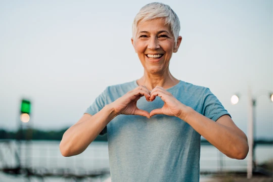 A woman smiling and holding up her hands to make a heart shape